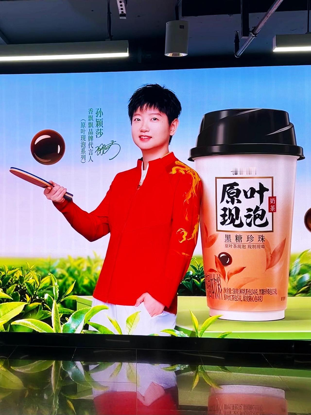 在上海，这样金贵的城市，香飘飘宣传孙颖莎，红色的队服，手持乒乓球拍，靠着香飘飘，