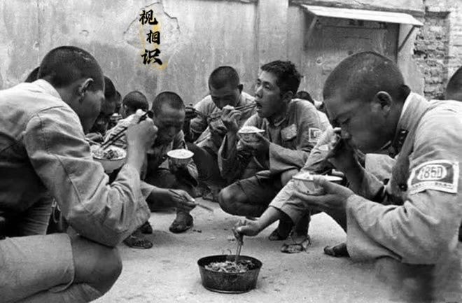 1939年，南昌会战前，战士们用餐的场景照片，画面中他们穿着简陋的军装和草鞋，一...