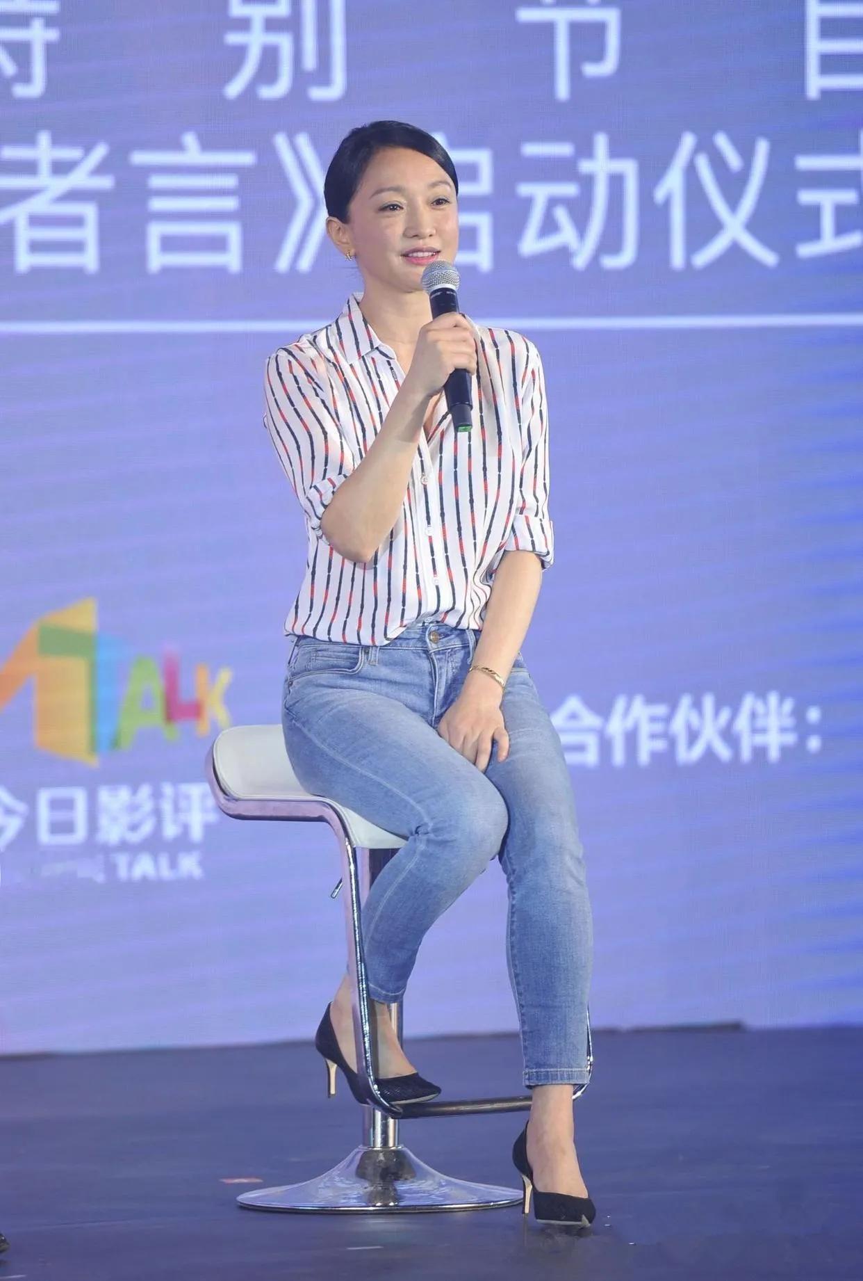 图片中的周迅白色衬衣，牛仔裤，黑色高跟鞋，坐姿优美。虽然这身妆扮比较简洁，给人一