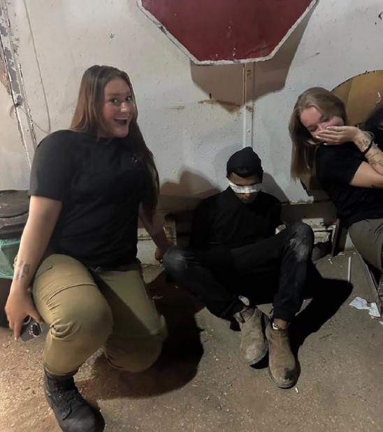 两名年轻的以色列女兵面带笑容，对着镜头开心地摆着姿势。然而就在她们身旁，却坐着一