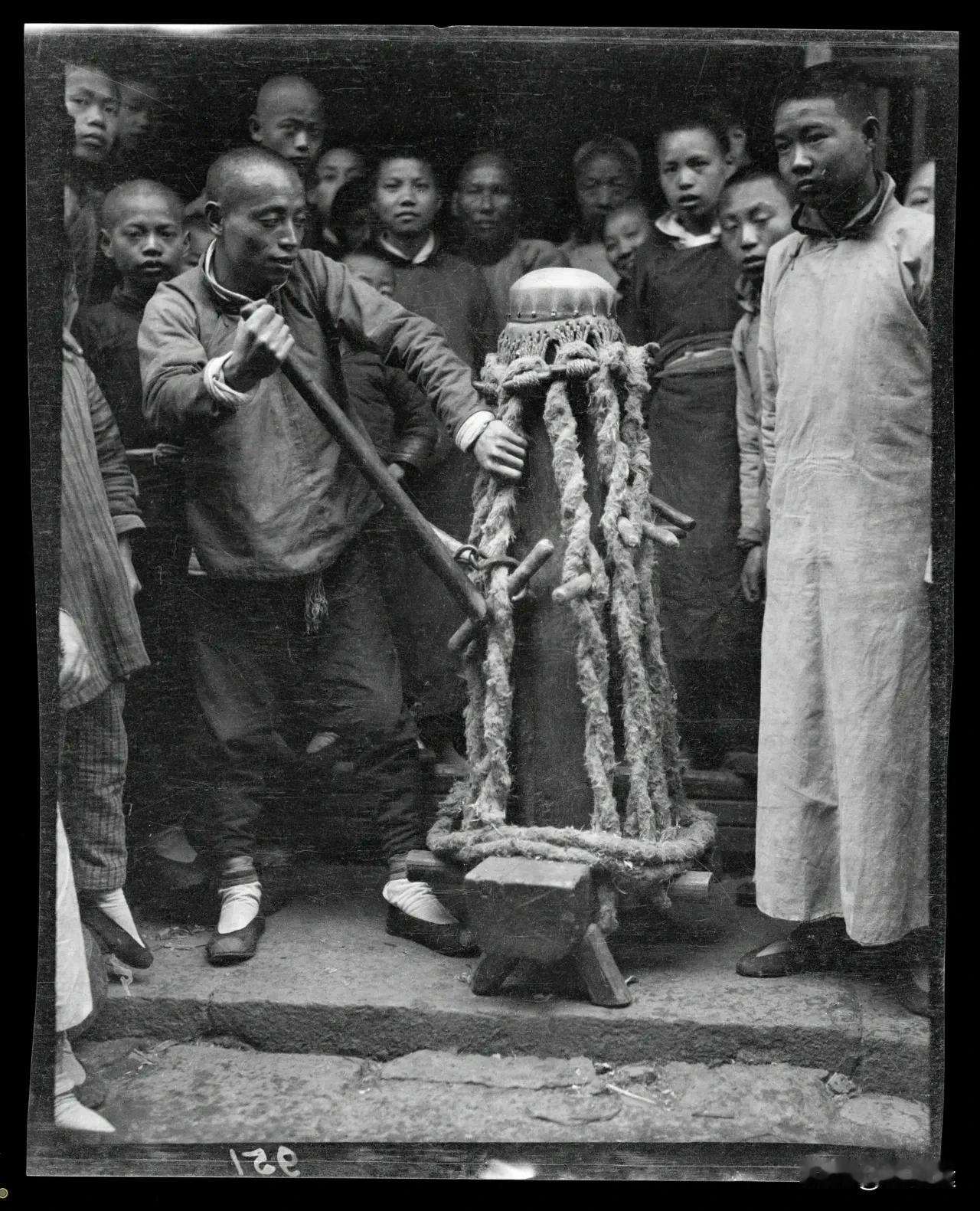 拍摄于1917年的中国，一群人在操作一种古老的榨油设备。榨油设备由一根木柱和多根