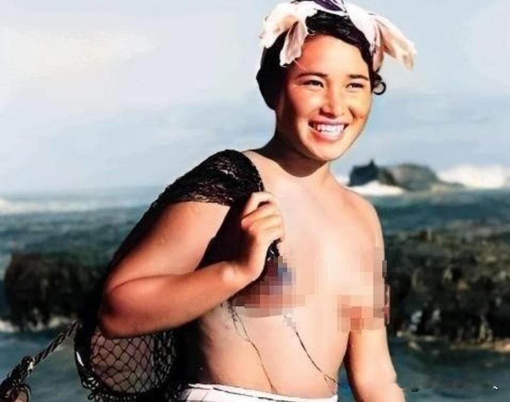 1955年，一名身体强壮的日本女人赤裸上半身，背着一个黑色的编织袋站在海边。这个