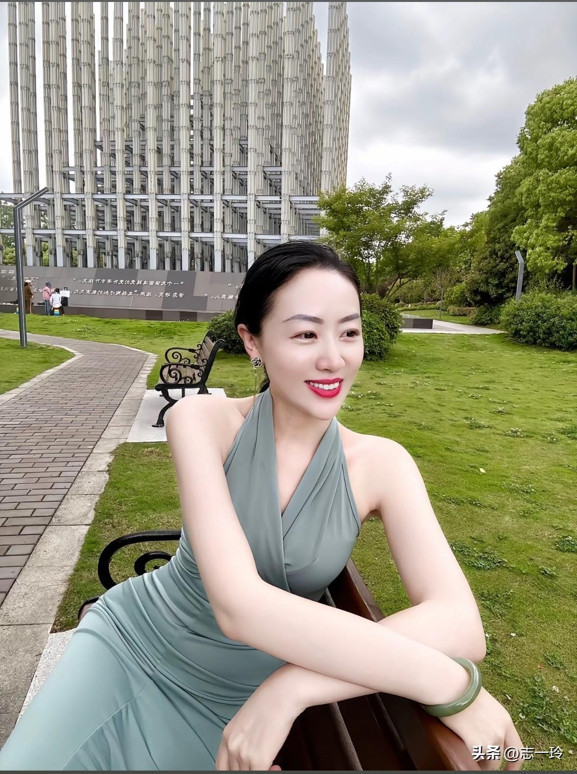 优雅绿裙女子，静坐公园长椅，微笑沉思，背景现代建筑。