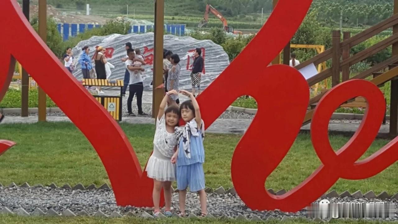两个小朋友在“Ye”字雕塑前开心玩耍，背景是欢乐的游乐场。晒晒随拍的湖光山色 户