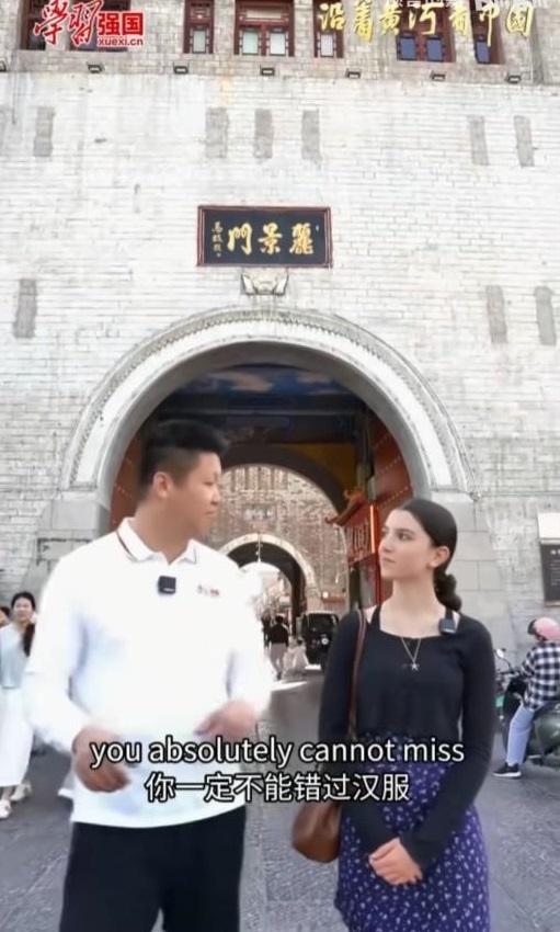 “学习强国”向外国女留学生讲解汉服。
看背景，是河南洛阳的丽景门。
女留学生是阿