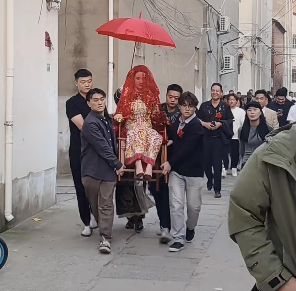 新娘坐在椅子上，戴着头纱，被娘家人打着伞抬着，不知道哪里的习俗，看上去还挺有古风