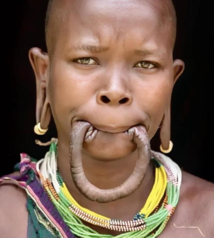这是一名漂亮的非洲“唇盘族”女孩，她嘴里含着的并不是香肠，而是自己的下嘴唇，女孩