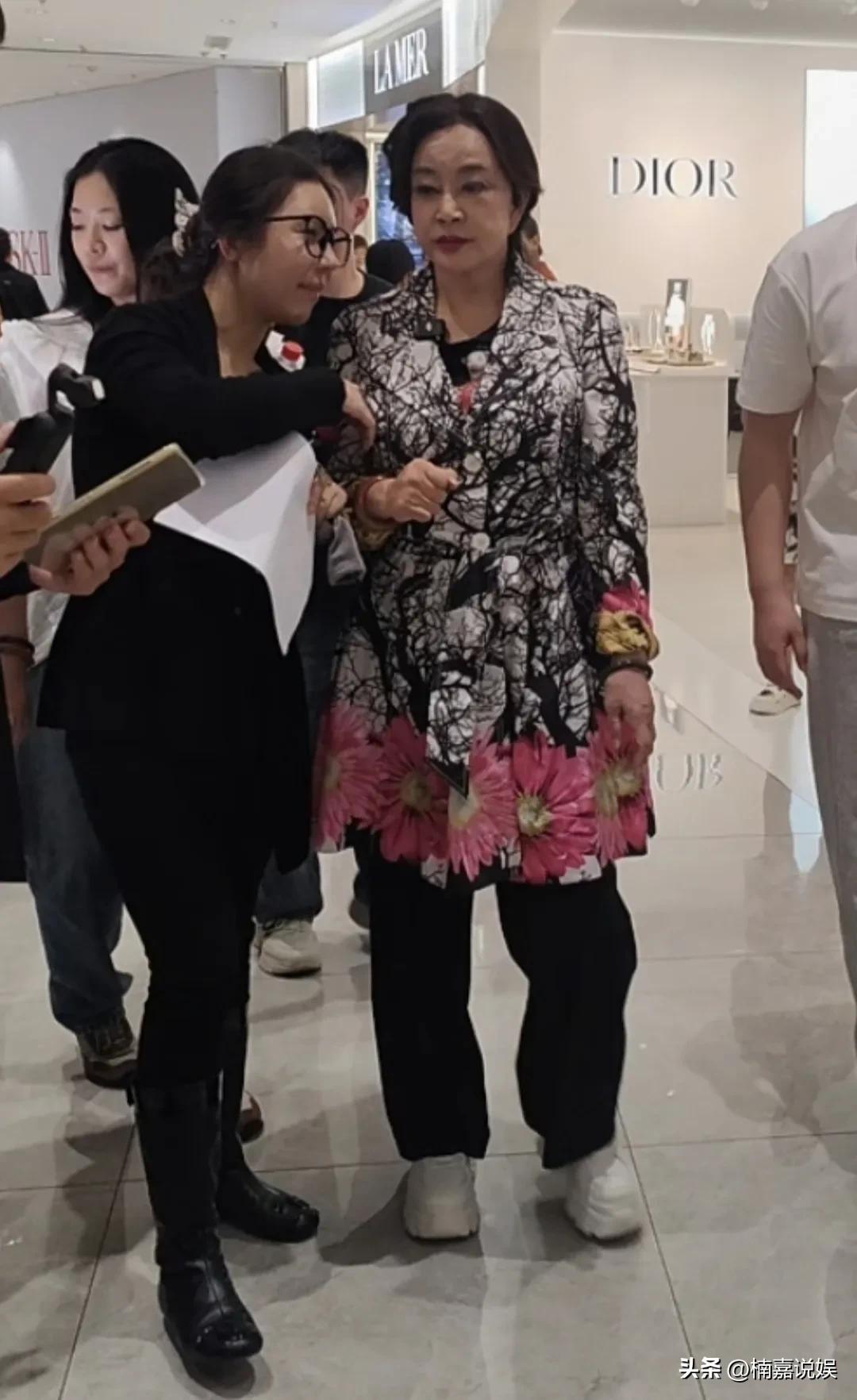 刘晓庆现身海南，穿着一件长花衣，黑色裤子，脚踩白色增高鞋，身材微胖，手上戴着一个