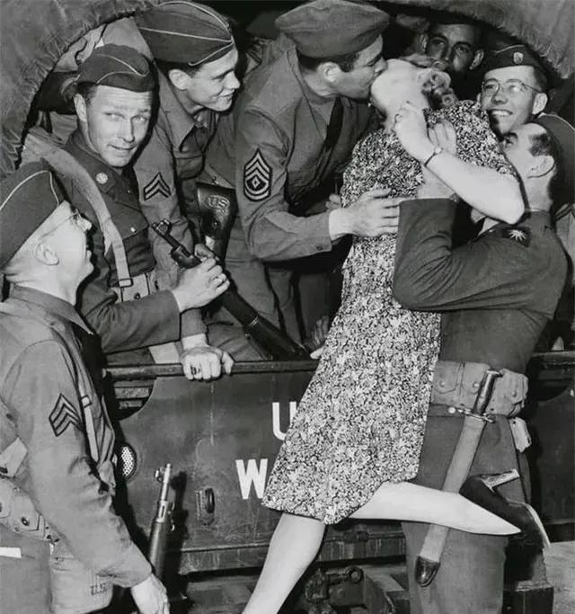 1940年，一名士兵举起一名年轻貌美的女人，将她送给卡车上的大兵，大兵见到女子不