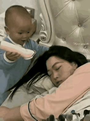 一个女人在家哄孩子，女人哄着哄着，她觉得有点困了，女人躺在床上，拿起一个被子盖在