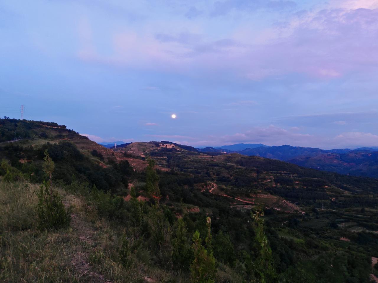 田野风景随手拍暮色缓缓笼罩连绵的黄土山峦，一轮圆月静静悬在淡紫渐变的天幕上，薄云