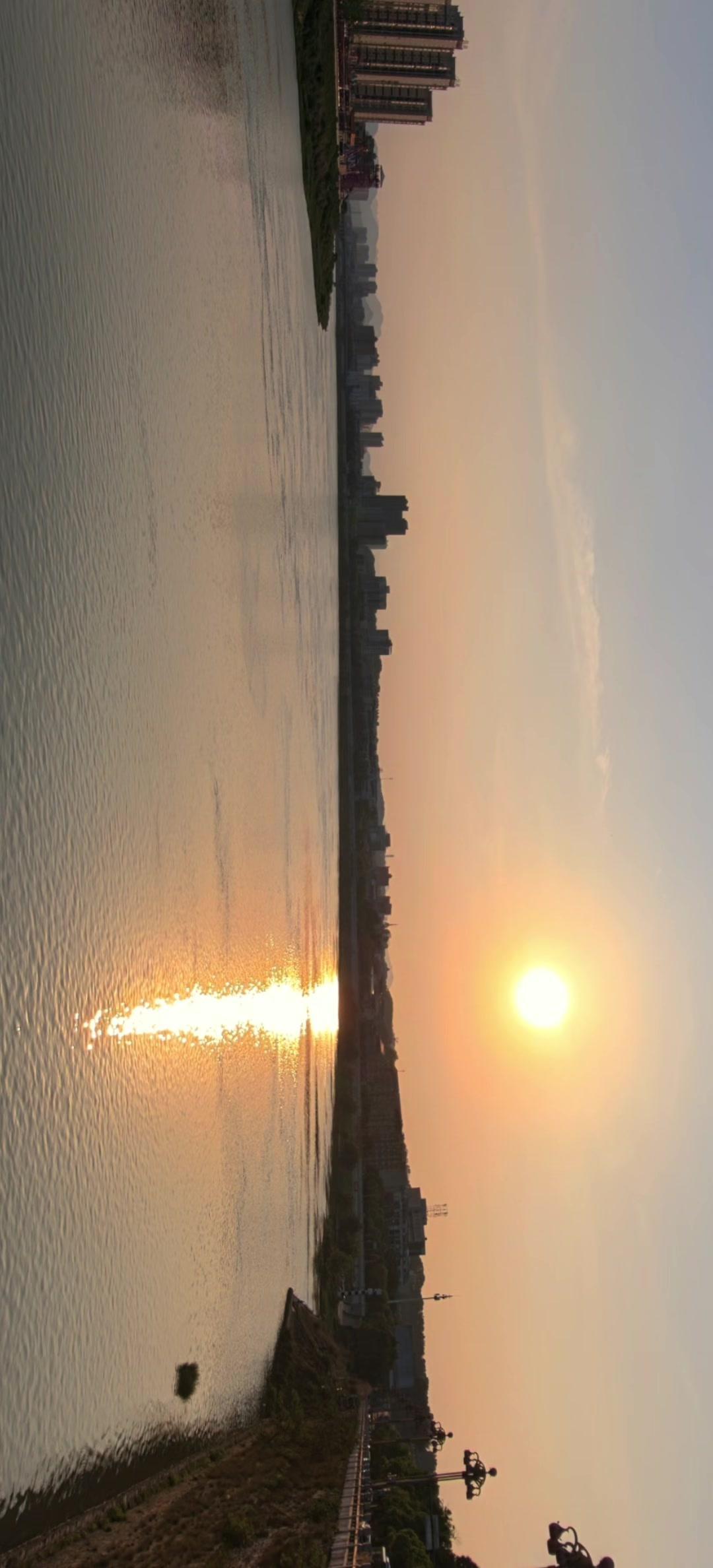 🌇城市天际线被橘色落日晕染，江水成了碎金镜子。路灯未亮，晚风裹着湿气掠过，远处