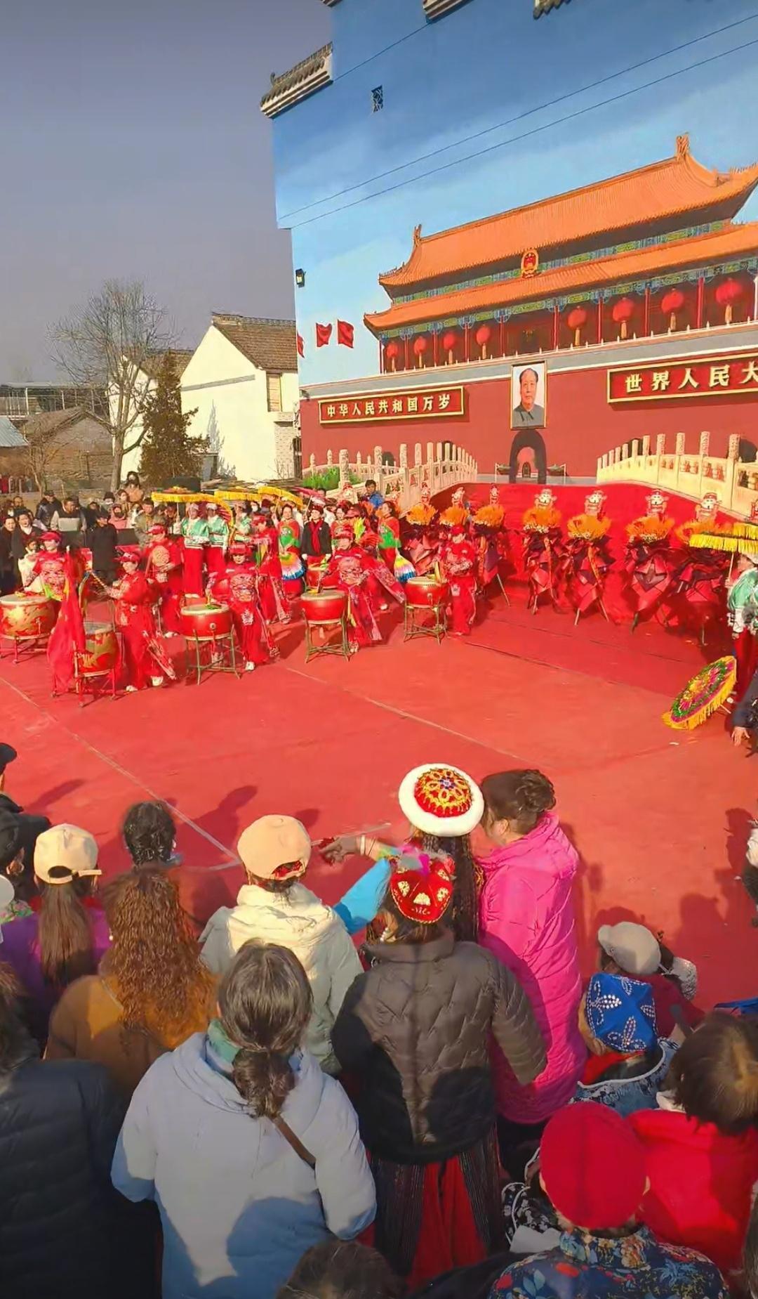 陕西宝鸡永利村的墙画开幕式举办得十分隆重。现场摆放着众多花篮，教员画像的安装尤为