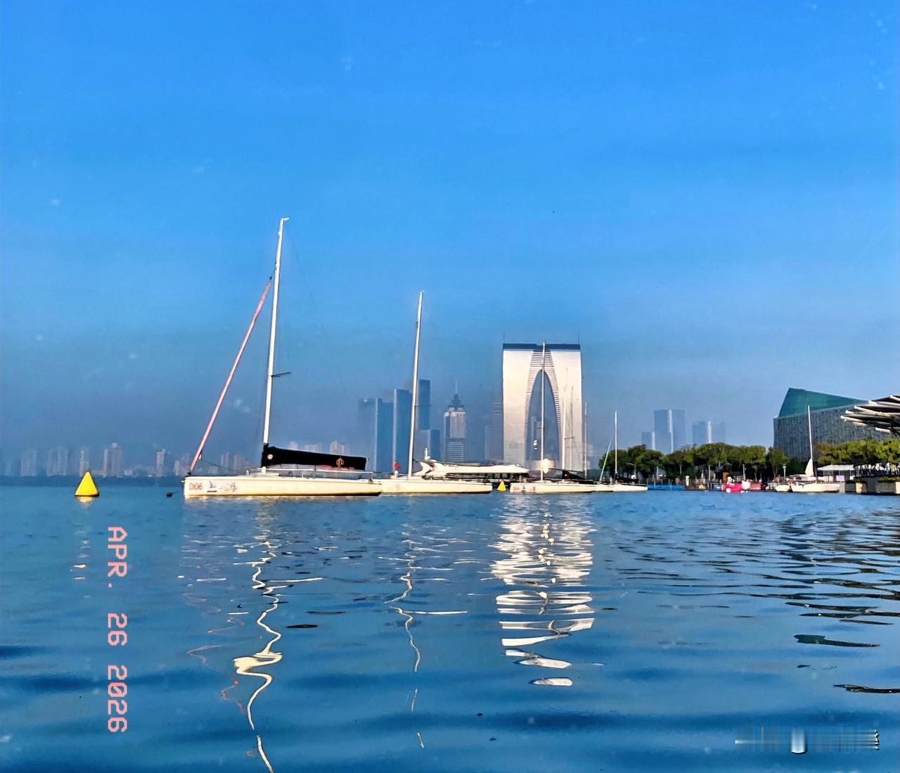 金鸡湖水蓝似海，
帆船点点印碧水。
微风轻拂皱涟漪，
湖畔繁花竞芳菲。
游人如织