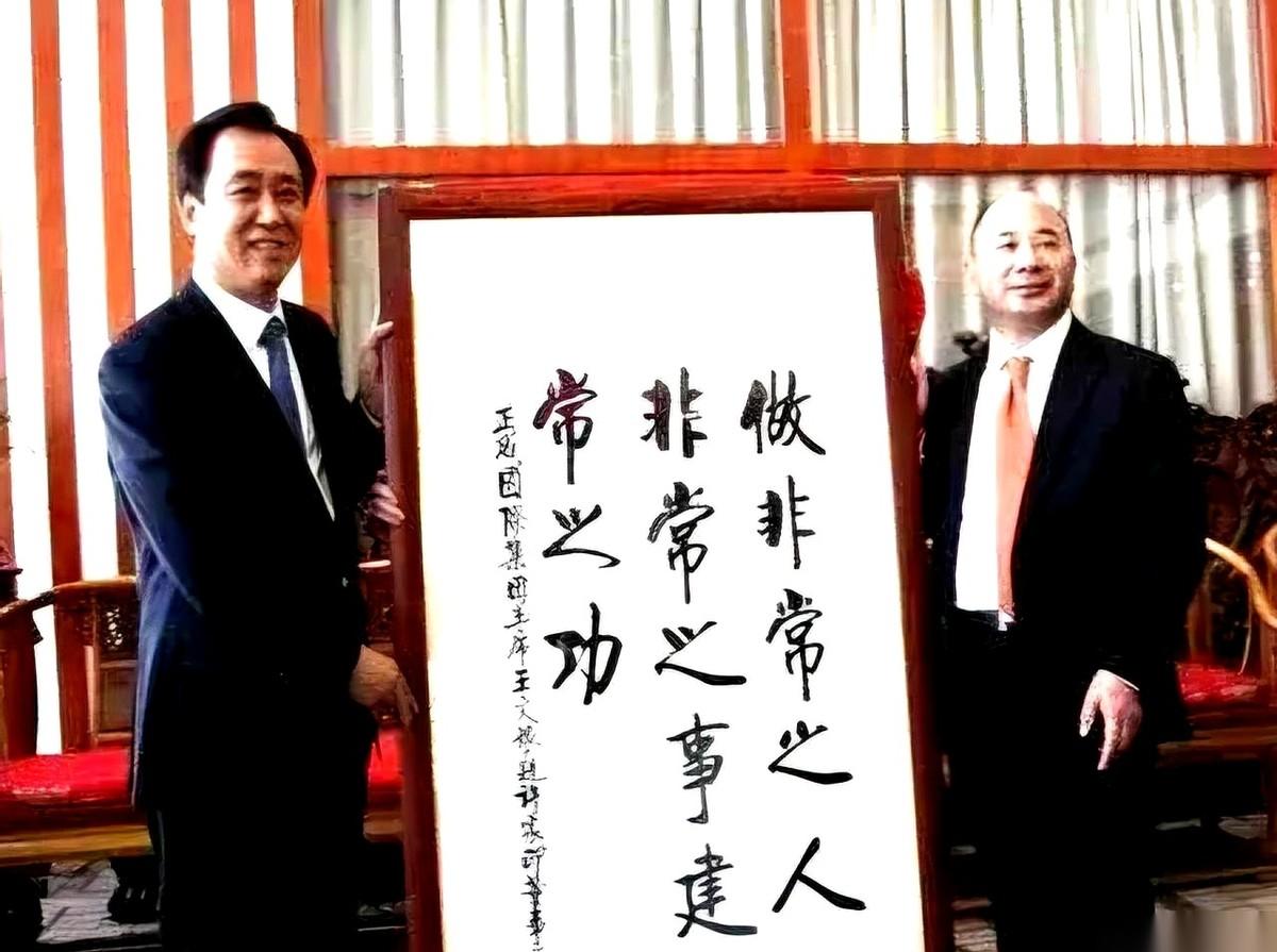 这张合影的主角是王文银和许家印。画面里，两个穿着挺括黑西装的男人各拽着宣纸的一头