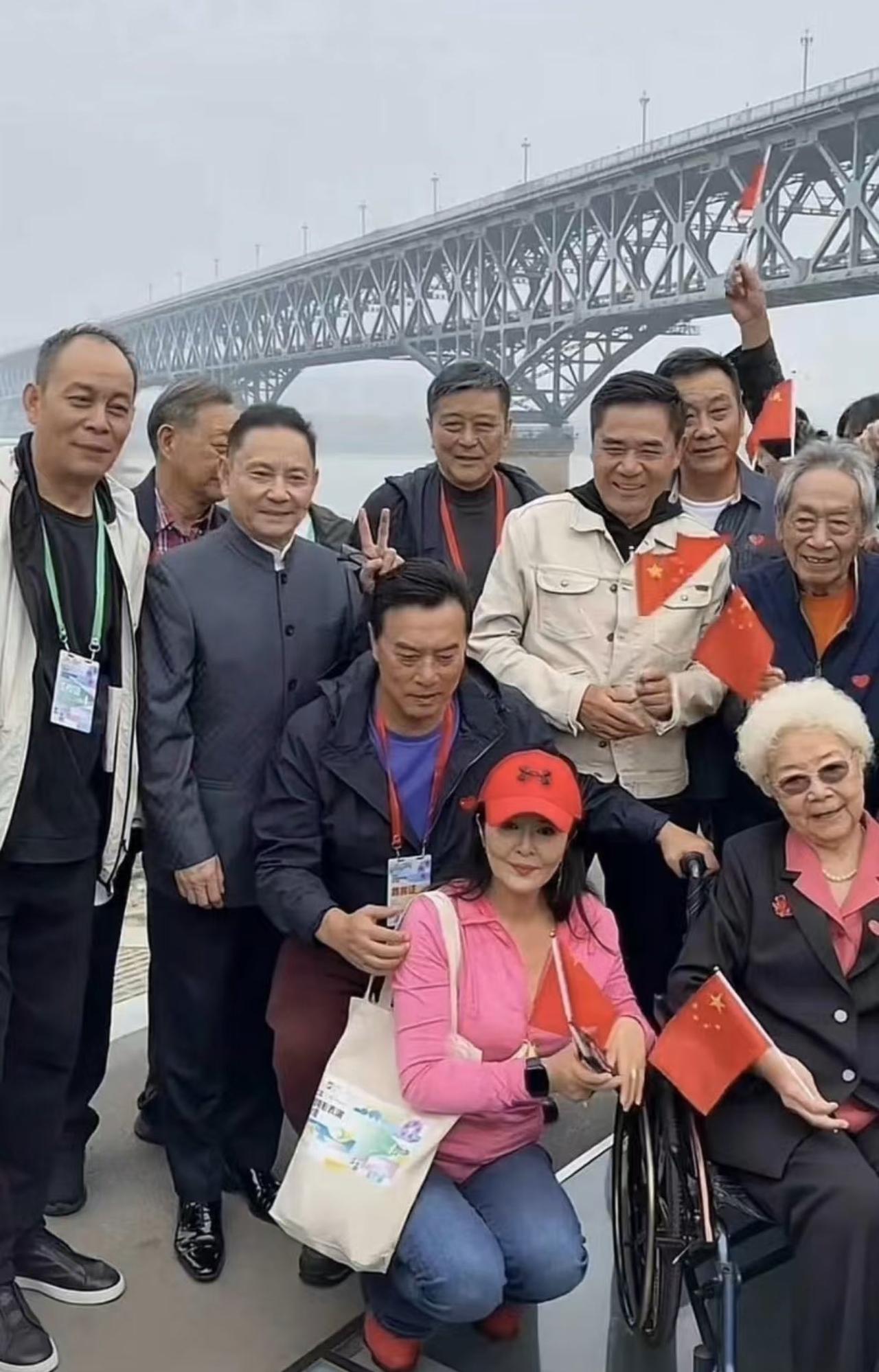 照片中一群老人及其随行人员在宏伟的南京长江大桥前手持中国国旗随意合影留念，初看之