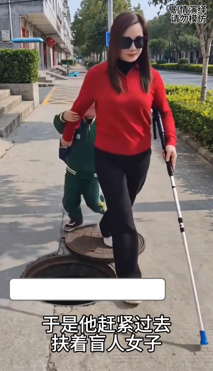 男孩暖心的帮助盲人女子。
盲人女子正在路上走着，这时刚放学的男孩看到下水道没盖，