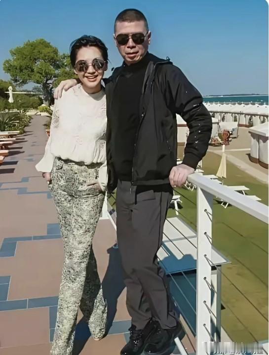 晴朗透亮的蓝天衬着远处碧蓝的海面，观景平台旁能看见成片草坪。许晴和冯小刚并肩站在