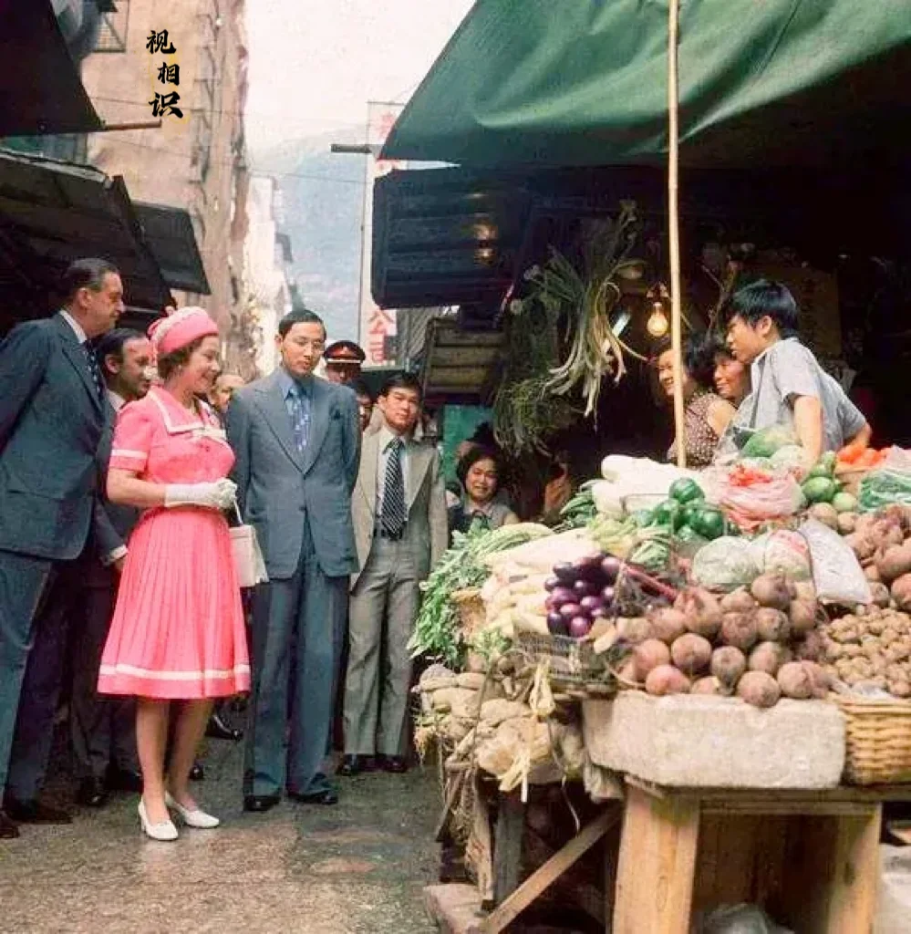 1975年，49岁的伊丽莎白女王首次访问香港，在中环嘉咸街菜市场，与摊主交谈时的...