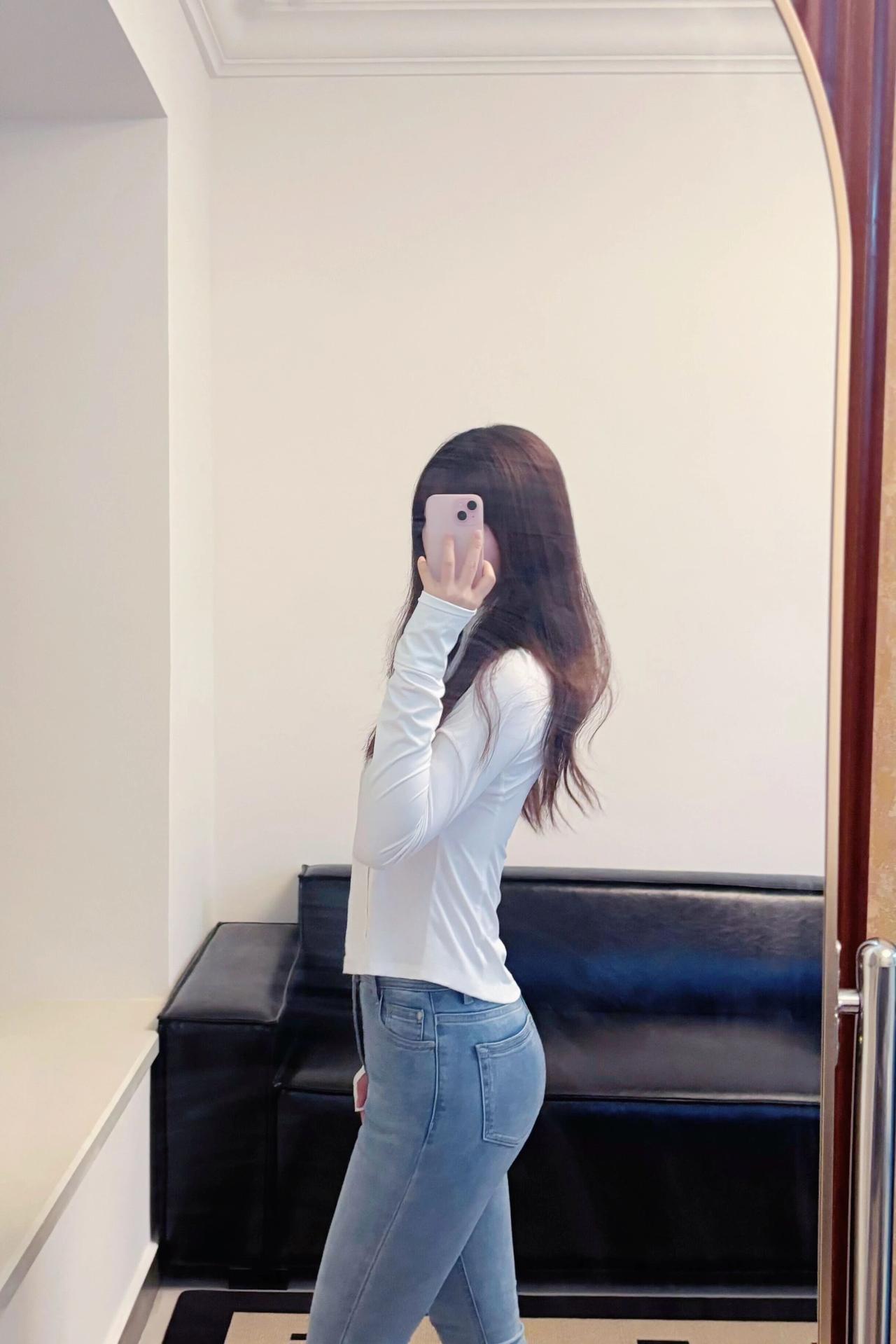 在镜子前自拍，穿白色上衣和牛仔裤。