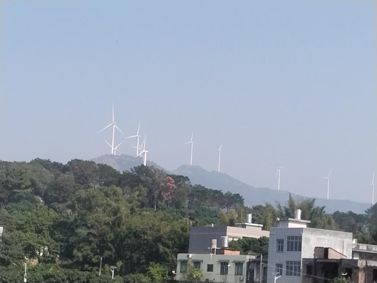 远山之上，一排排白色风车叶片正随风缓缓转动，与蓝天白云相映成景。这些风力发电机不