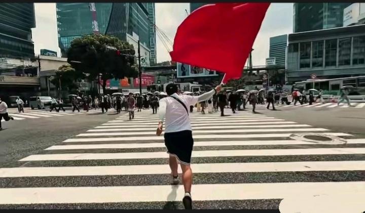 一名中国小伙子挥舞着一面巨大的五星红旗，在日本的一条大街上高调行走。
     