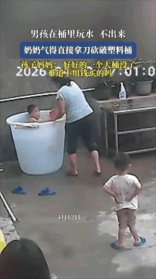 男孩在一米高的水桶里玩水，奶奶看着太危险，喊他赶紧出来。但是男孩并不领情，奶奶无