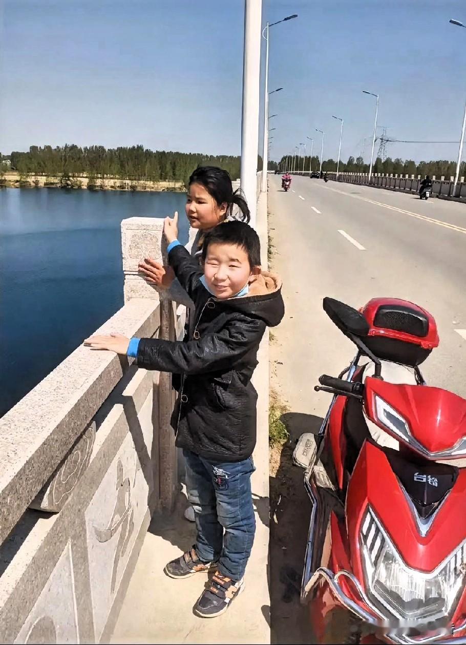两个孩子在桥边看风景，旁边停着一辆红色摩托车。
