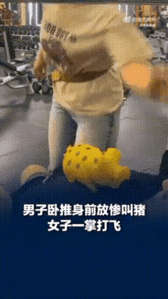 男子在健身房练卧推时，一女子正在旁边练深蹲，
男子为了缓冲在胸口放了一个惨叫猪。