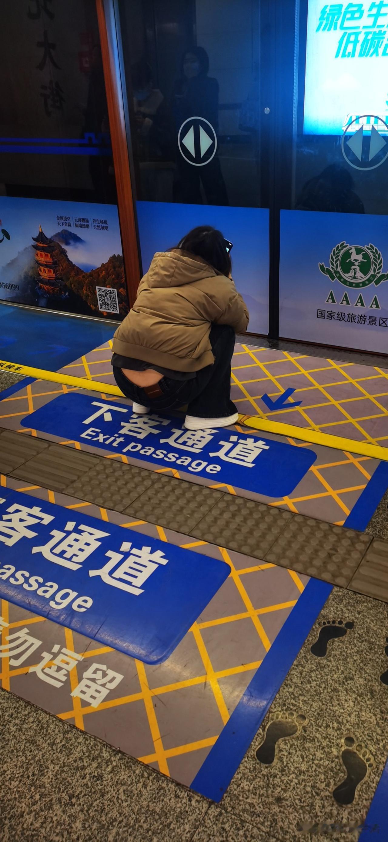 今早西安地铁1号线，这位姑娘蹲在下客通道正中间看手机，旁边就是“勿逗留”的标识。