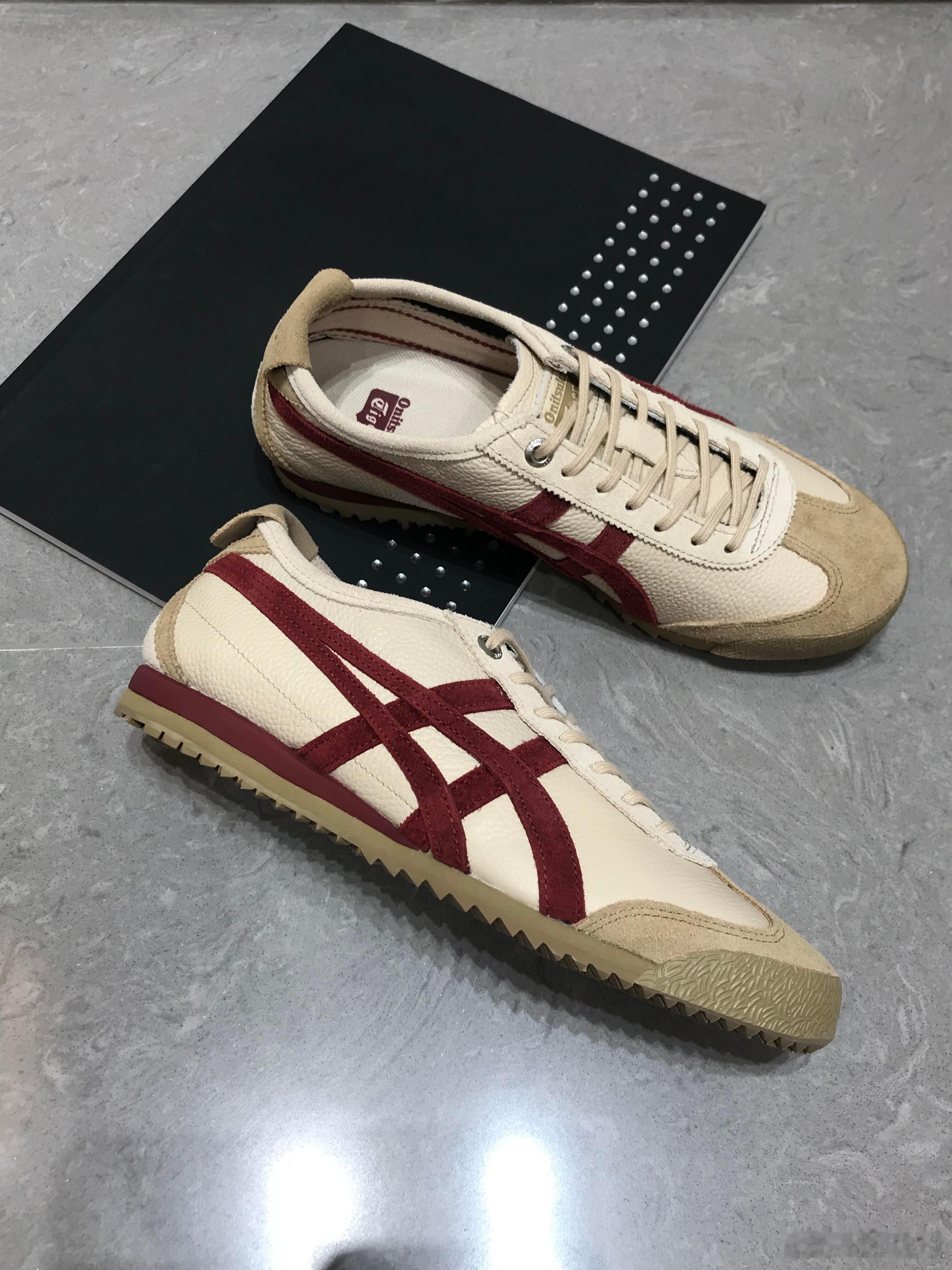 这双Onitsuka Tiger经典运动鞋以米白色皮革鞋面为主，搭配标志性的酒红