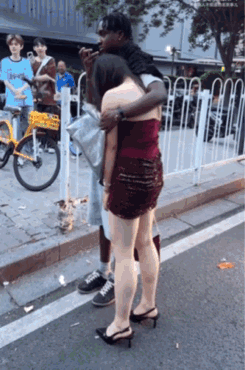 一黑人男子搂着一名年轻女子。只见这名女子站在原地一动不动，把头埋在男子怀中，一开