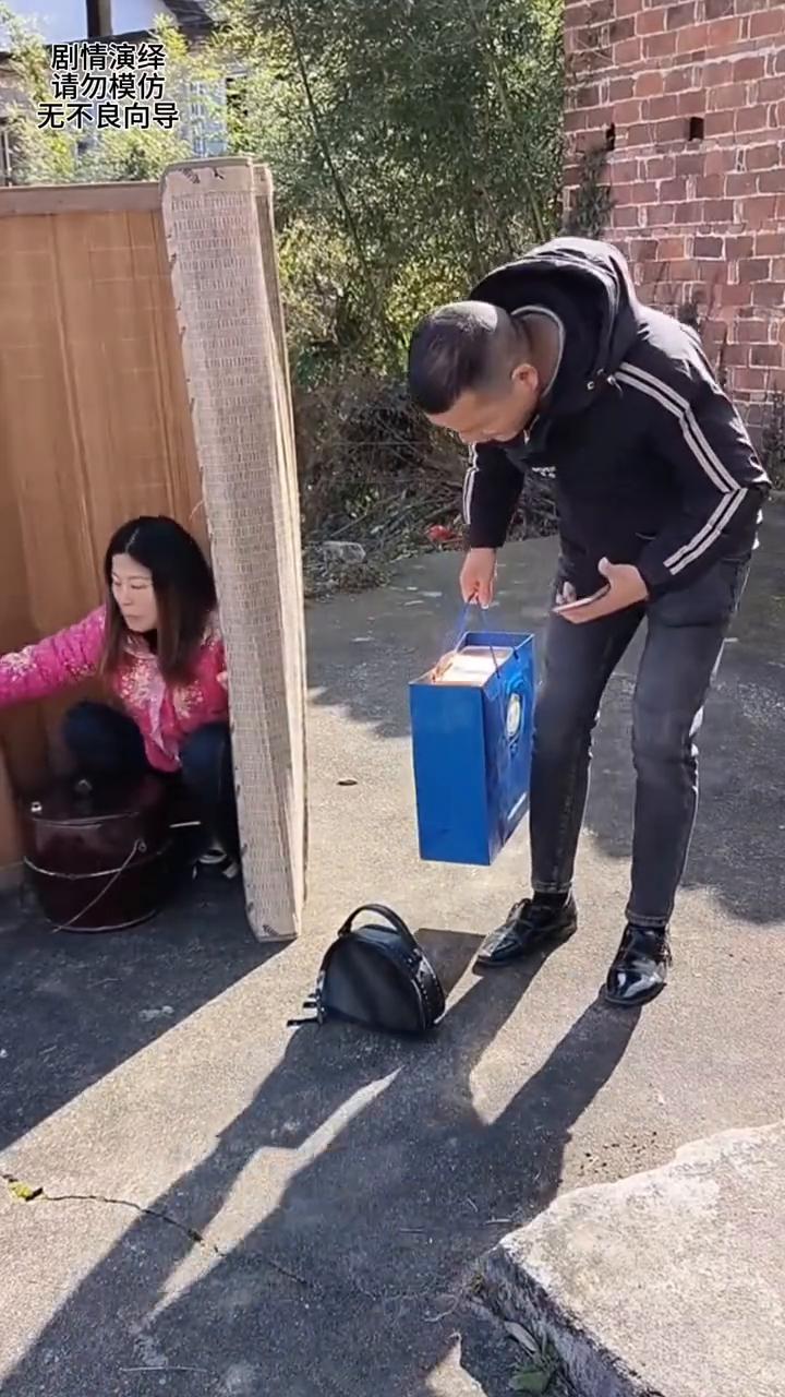 女子为了整蛊一下男子，只见他看着手机提着东西走过来，随后女子把包扔到路上。就当男
