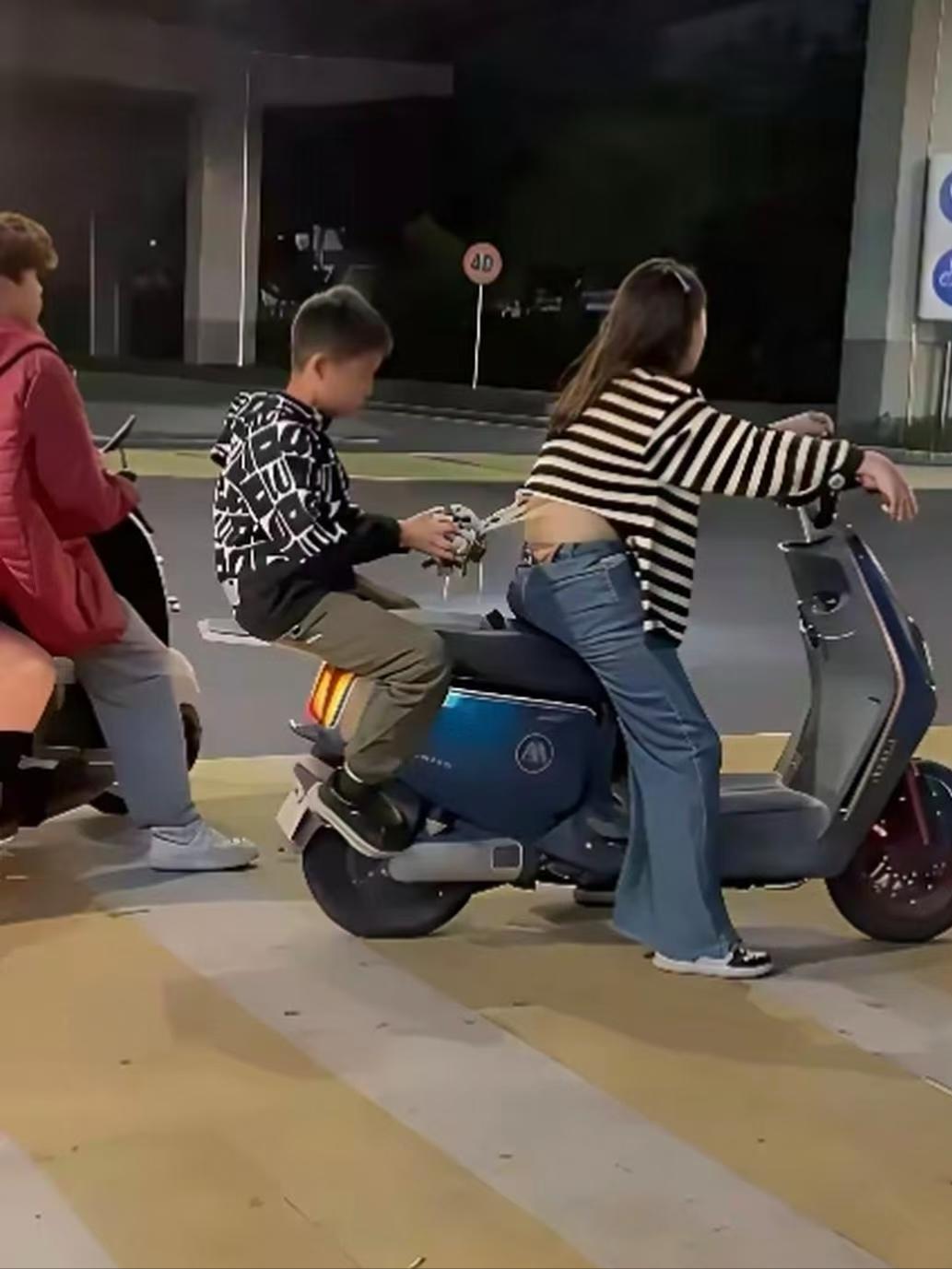 夜色里的小电驴旁，男孩手里的小玩具，偷偷戳中了后座的 “小调皮”~