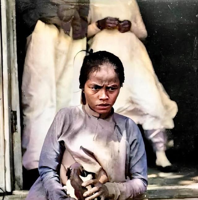 1880年，越南河内，一名年轻的越南女子正在用自己的母乳喂小狗。她坐在门前的石阶