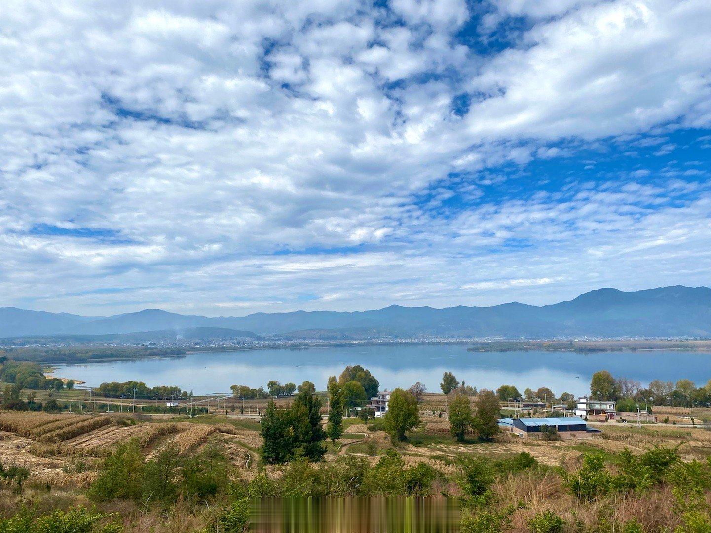 深秋初冬的大理剑川剑湖，水色澄澈，水岸层林尽染，周边山峦叠嶂，白族村落炊烟袅袅，