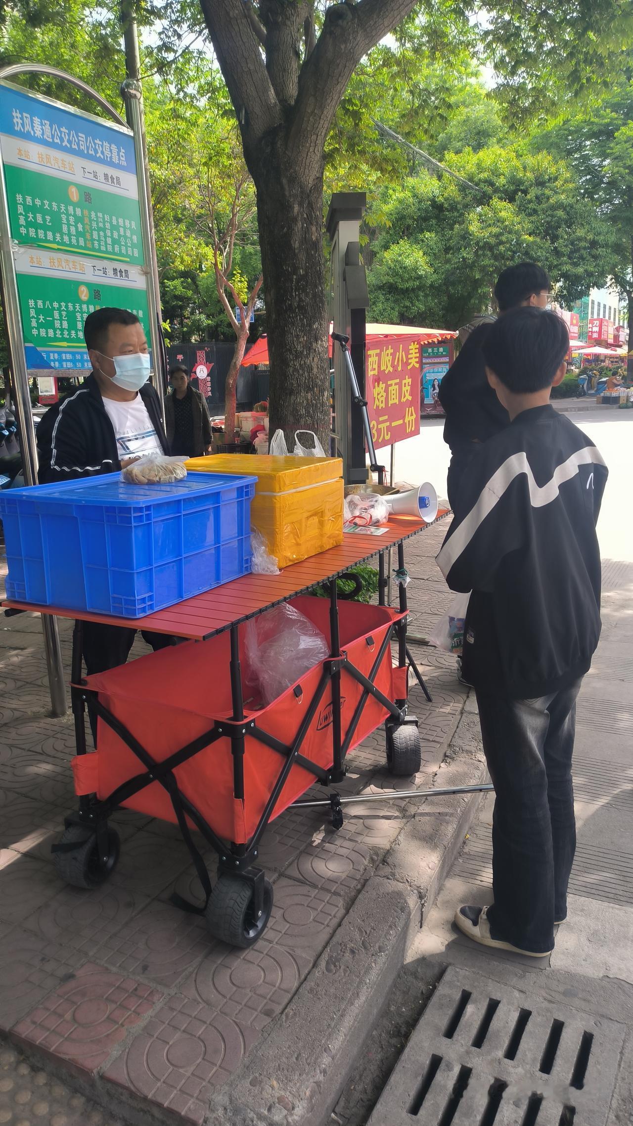 从扶风气车站出来。看到马路对面公交站牌前支着一个摊。摊位上有直播设备。走到跟前一