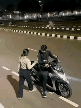 小伙子骑摩托车准备载女朋友出去兜风，当女孩要跨上摩托车时，男朋友故意逗她，往前开