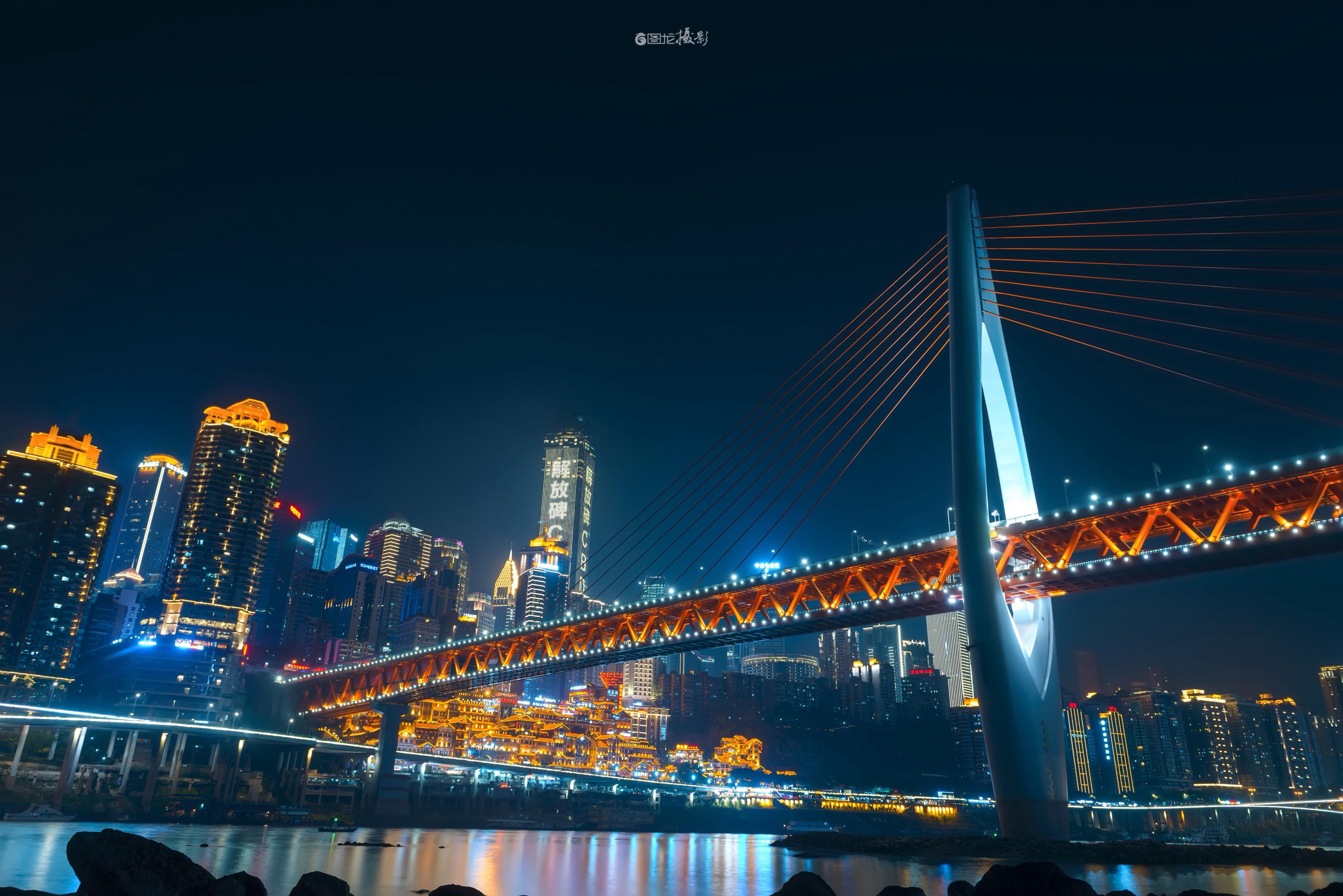 重庆的夜之交响：桥与城的光影狂想。在重庆的夜幕下，一座斜拉桥如金色的竖...