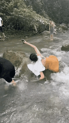 果然是保手机更重要，女子都滑进河里了，手机还高高举在空中！
河道中的石头滑得很，