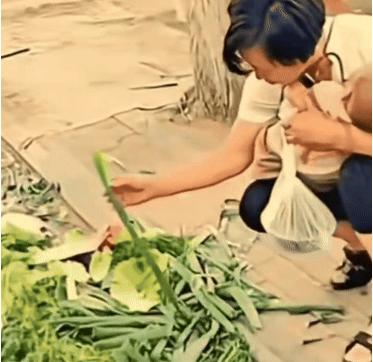 “让人心酸！”一女子不顾周围人的目光，抱着熟睡的孩子，蹲在路边捡别人不要的生菜叶