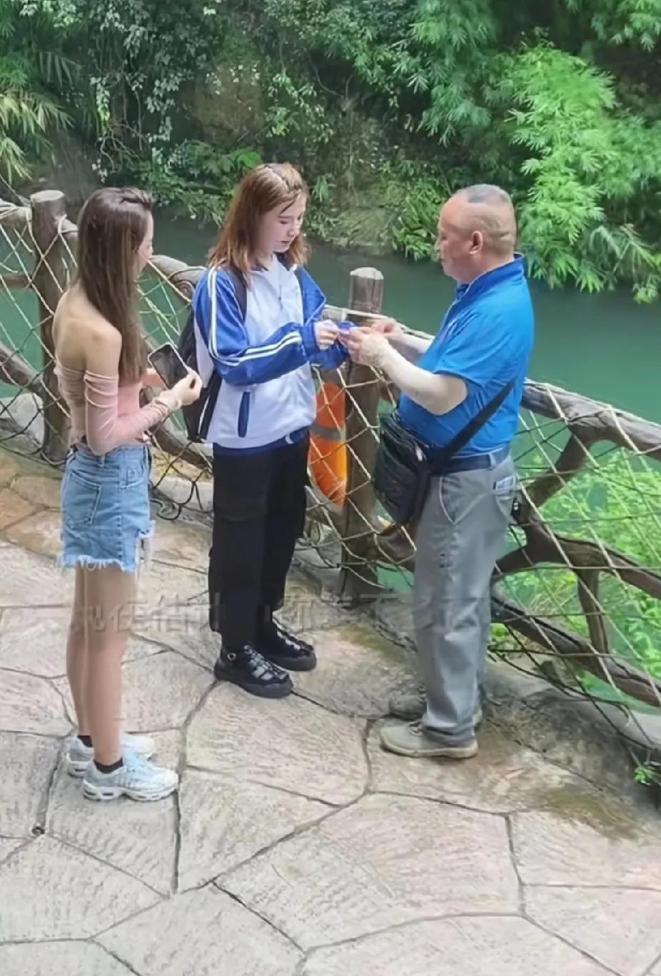 两个女孩站在景区的瀑布前拍照时，一位老人站在不远处一直盯着女孩看，一个女孩气冲冲