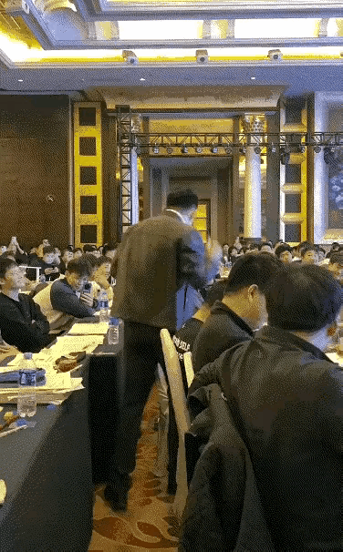 看着场景，像是在会议室，这个人手里拿着麦克风，态度相当的嚣张，现场就开始打人，也