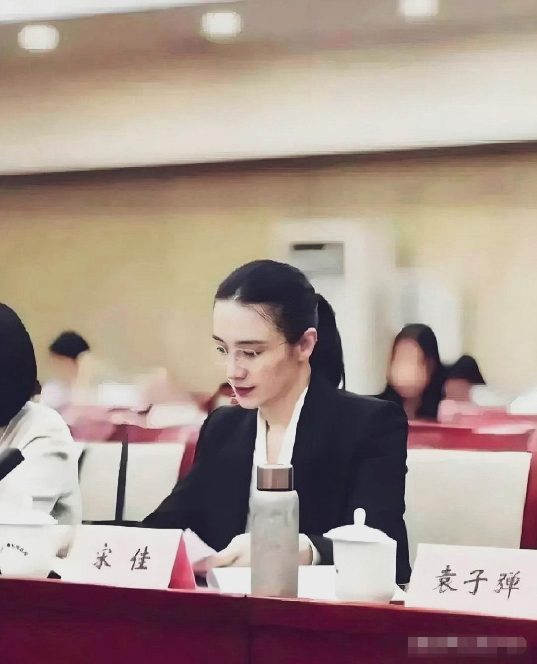 宋佳佩戴眼镜低头查阅文稿；姿态很有文艺范儿。身旁姓名牌可以看到袁子弹。