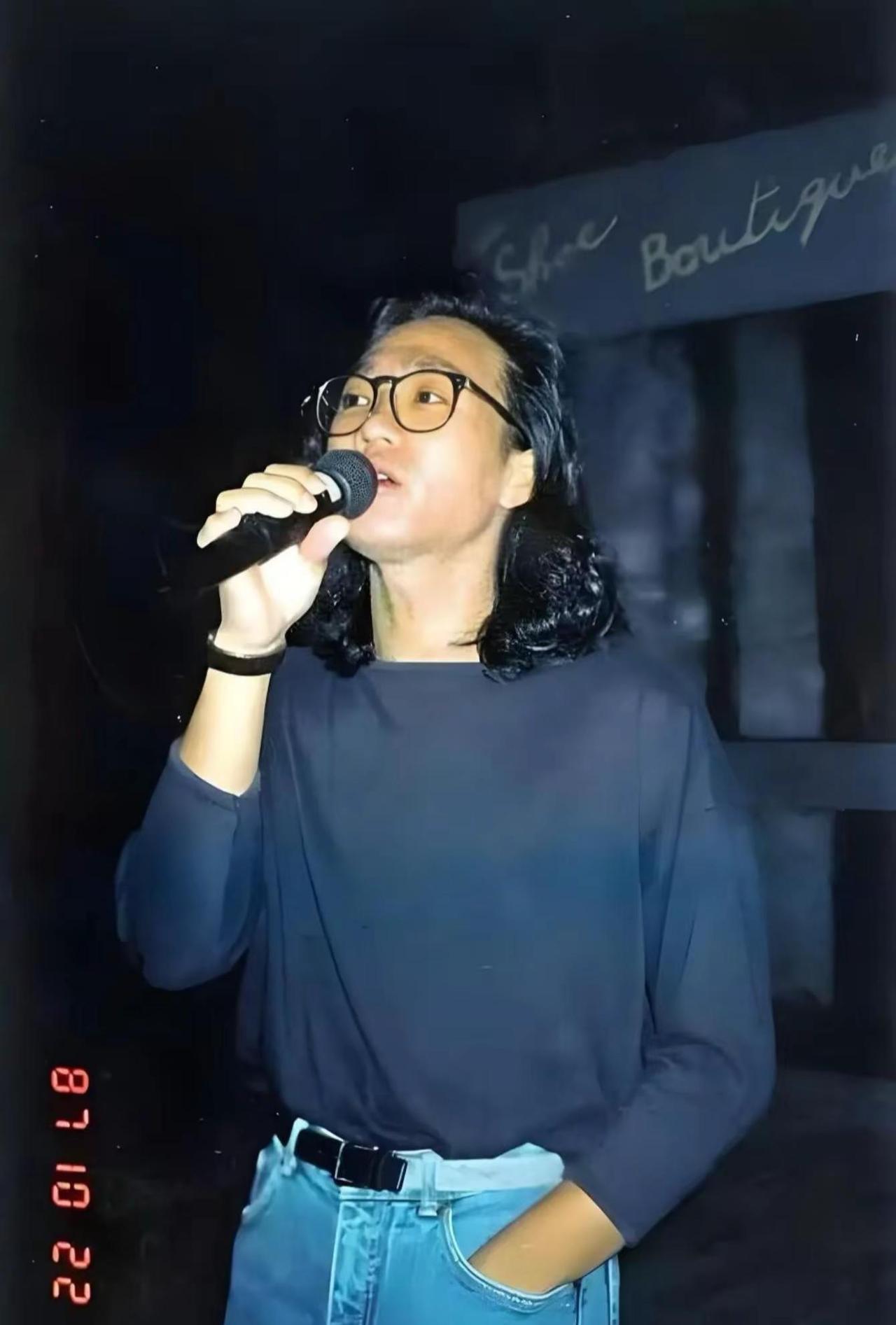 时间：1987年10月22日。照片里的家驹留着标志性的长发，佩戴黑框眼镜，正手持