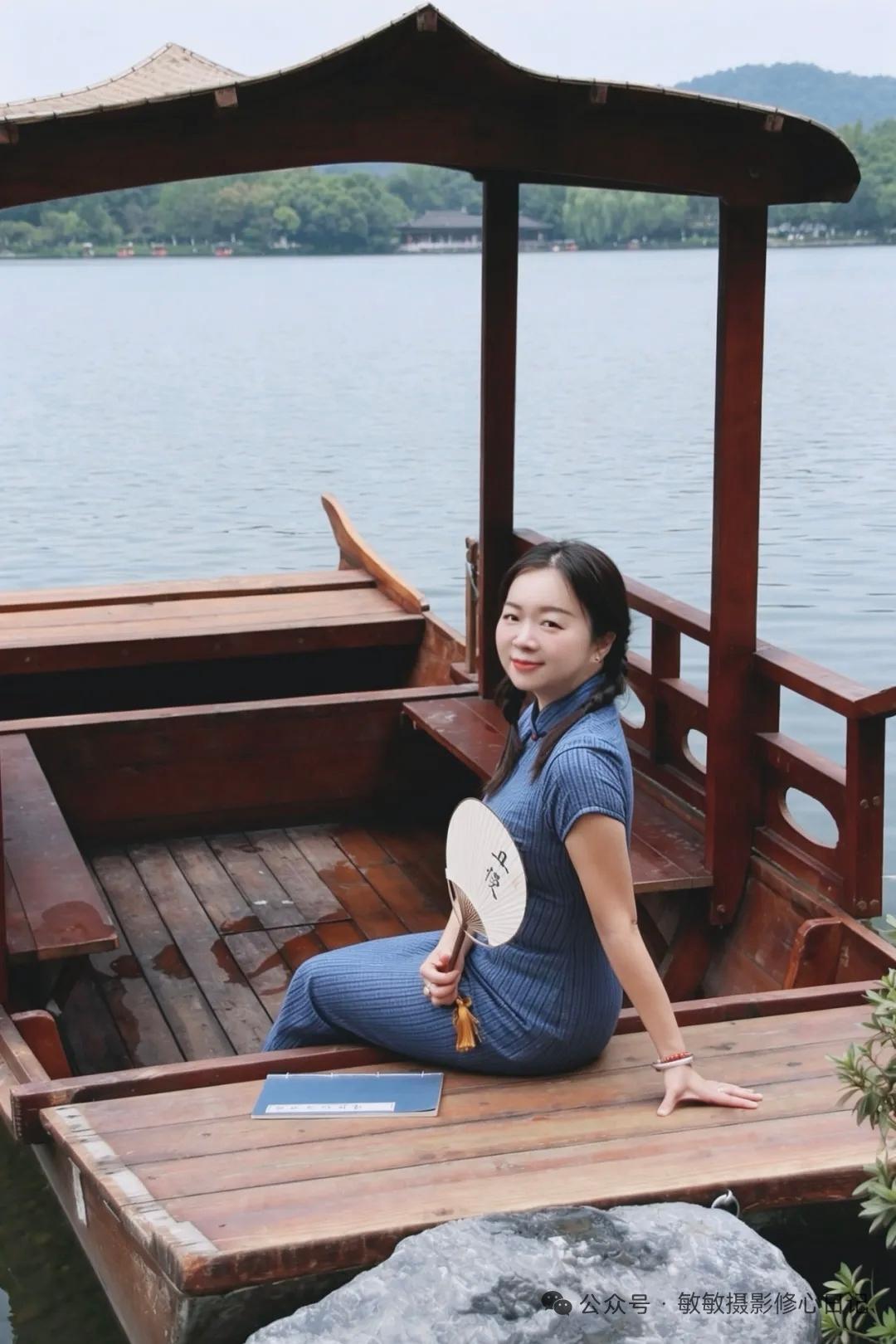 一位女士在湖边的木船上坐着，手持折扇。