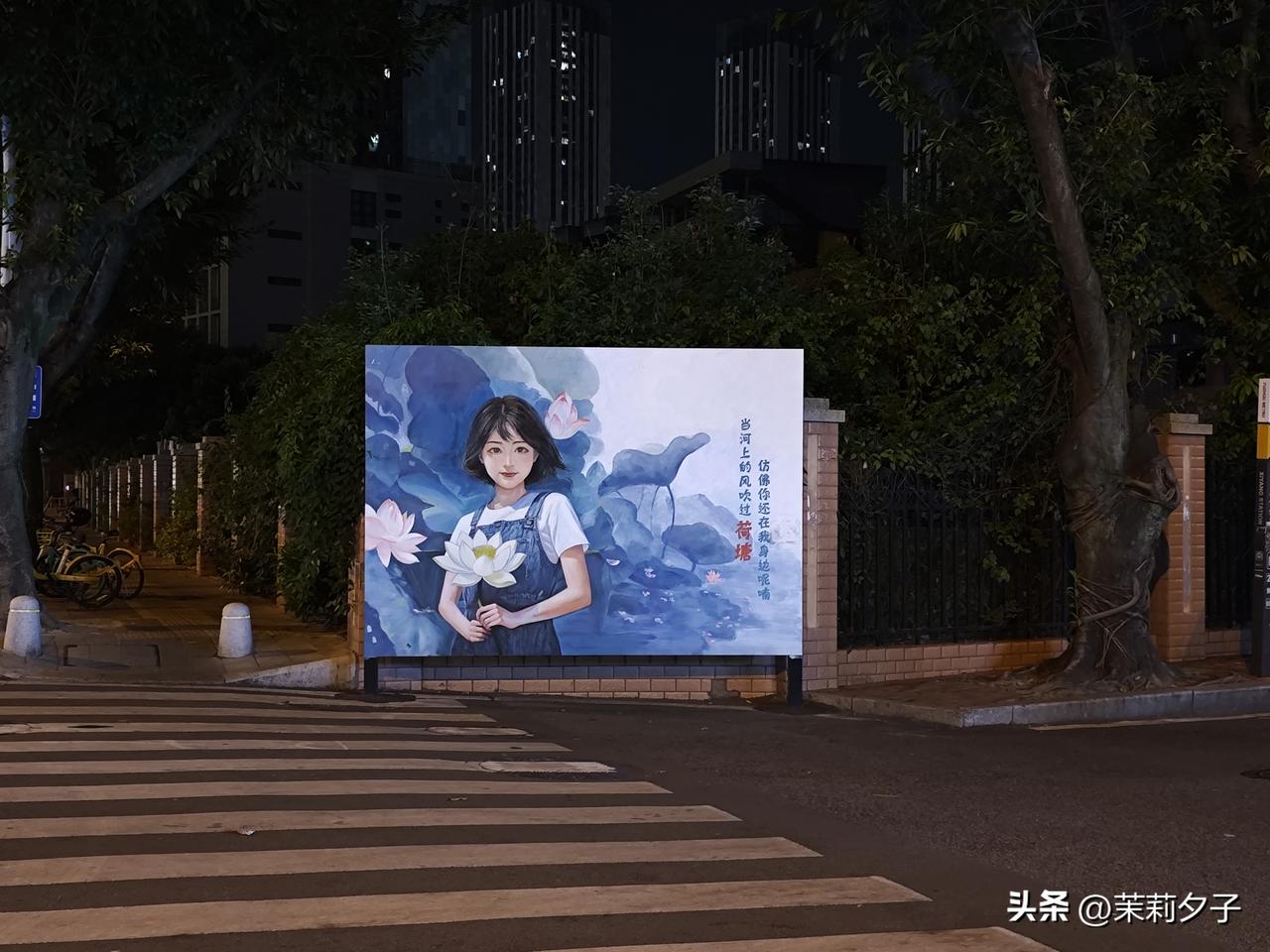 福州荷塘路，路口立着少女手持茶花的艺术画，街口的电箱也绘满荷花元素。看得出人造景