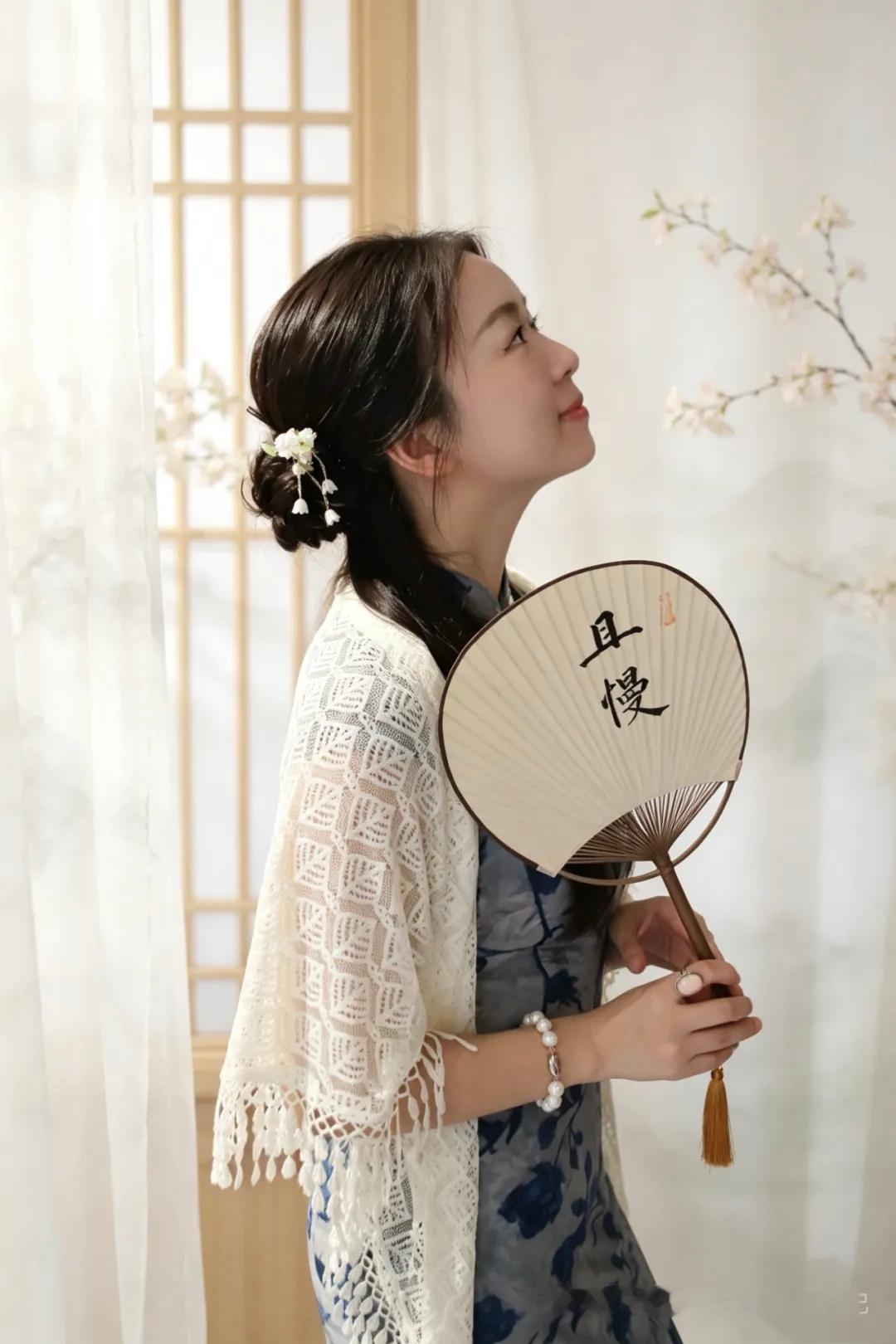 一个女孩拿着扇子，看向窗外。