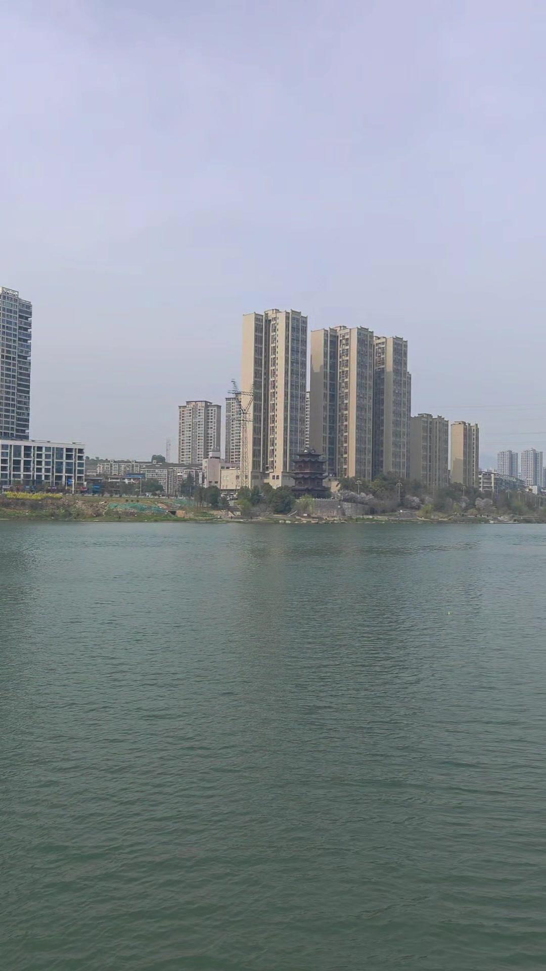 江岸边，澄澈江水静静流淌，水波粼粼。江岸景致相映成趣，现代高层住宅楼挺拔林立，是