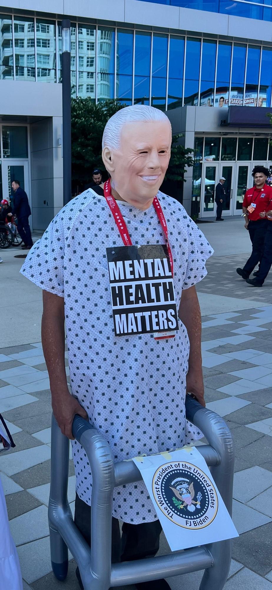 美国共和党人聚集在会场外真会玩。
有一个打扮成拜登的男人，穿着病号服和齐默框架，